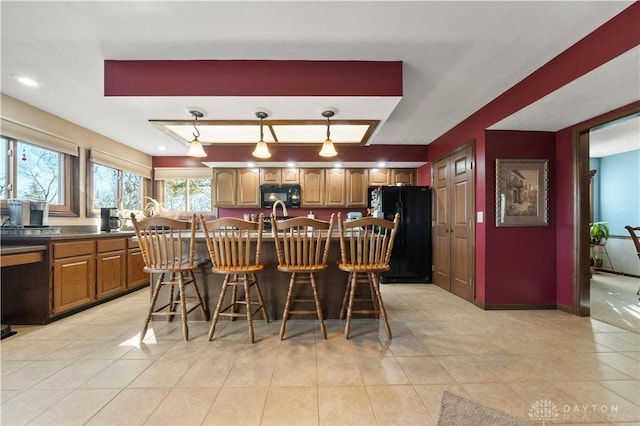 kitchen featuring light tile patterned flooring, a kitchen bar, hanging light fixtures, black appliances, and a center island with sink