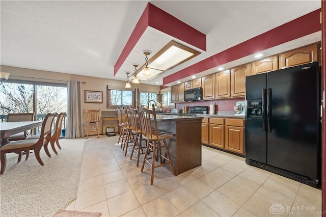 kitchen with hanging light fixtures, a kitchen breakfast bar, a center island, black appliances, and light tile patterned flooring