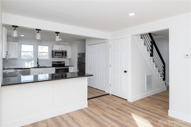 kitchen featuring sink, appliances with stainless steel finishes, white cabinetry, kitchen peninsula, and light wood-type flooring