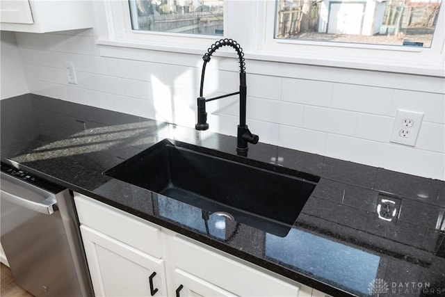 details featuring sink, tasteful backsplash, dark stone countertops, stainless steel dishwasher, and white cabinets