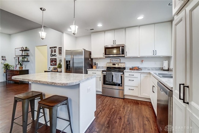 kitchen with sink, hanging light fixtures, a kitchen island, stainless steel appliances, and white cabinets