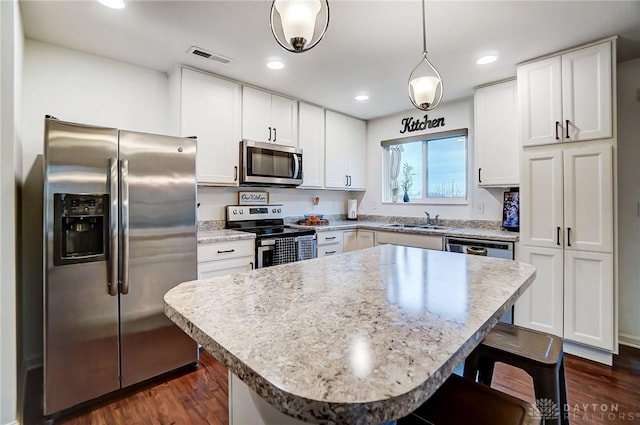 kitchen featuring a kitchen bar, white cabinetry, a center island, hanging light fixtures, and appliances with stainless steel finishes