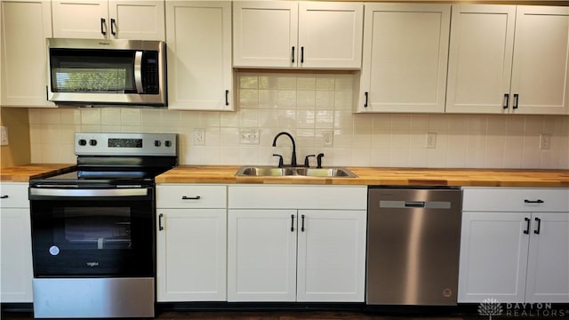 kitchen with appliances with stainless steel finishes, tasteful backsplash, white cabinetry, sink, and wooden counters