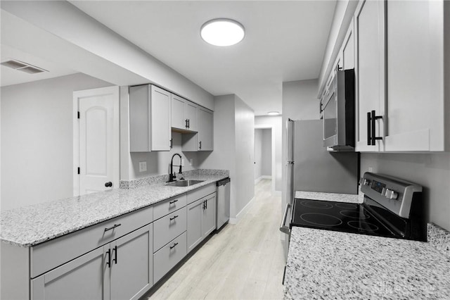 kitchen with gray cabinets, sink, light hardwood / wood-style floors, stainless steel appliances, and light stone countertops