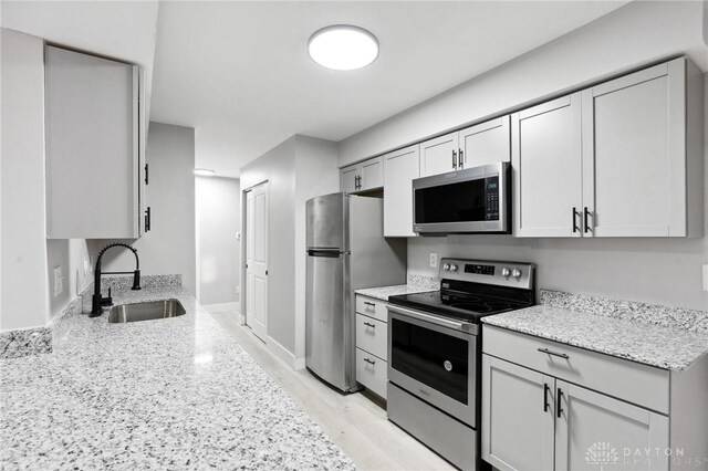 kitchen featuring light stone countertops, appliances with stainless steel finishes, sink, and light hardwood / wood-style floors