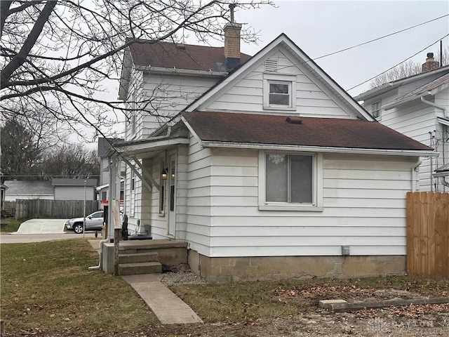 view of front of property with a shingled roof, a chimney, and fence