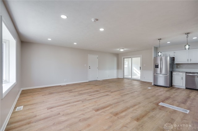 kitchen with white cabinetry, hanging light fixtures, light wood-type flooring, appliances with stainless steel finishes, and backsplash