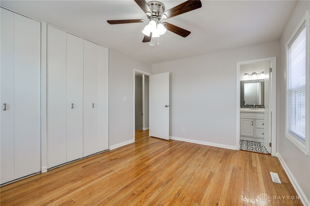 unfurnished bedroom featuring multiple windows, ensuite bath, light hardwood / wood-style floors, and ceiling fan