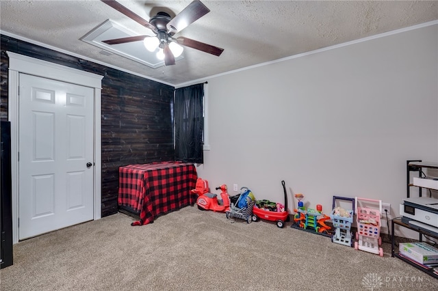 recreation room with wood walls, crown molding, a textured ceiling, carpet flooring, and ceiling fan