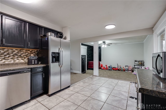 kitchen with light tile patterned flooring, backsplash, dark stone counters, ceiling fan, and stainless steel appliances