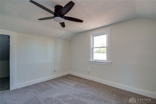 empty room with ceiling fan, lofted ceiling, carpet floors, and a textured ceiling