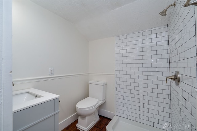 bathroom with tiled shower, vanity, toilet, and vaulted ceiling