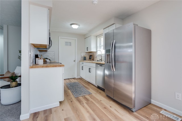 kitchen featuring appliances with stainless steel finishes, tasteful backsplash, sink, white cabinets, and light wood-type flooring