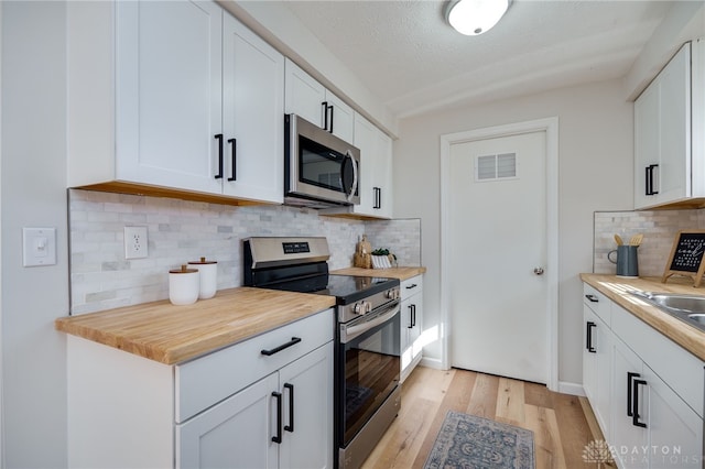 kitchen featuring white cabinetry, a textured ceiling, light wood-type flooring, appliances with stainless steel finishes, and decorative backsplash