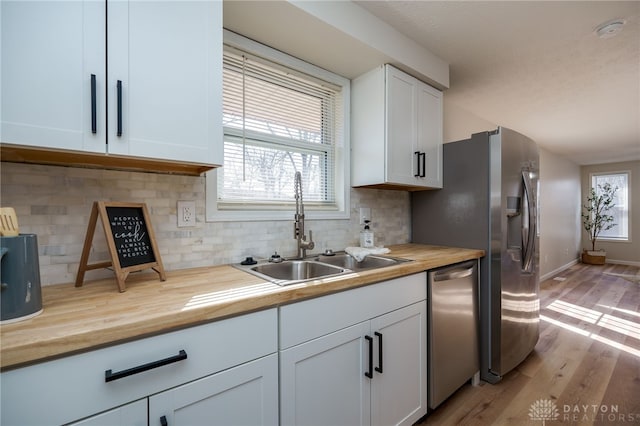 kitchen with a wealth of natural light, wood counters, sink, white cabinets, and stainless steel appliances