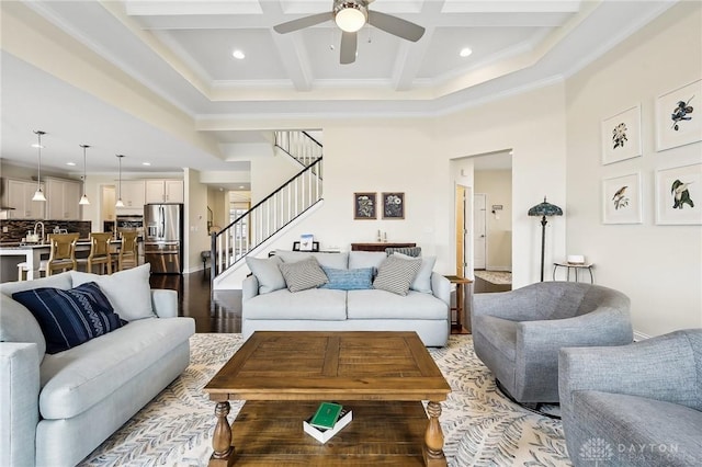 living room with coffered ceiling, a ceiling fan, stairs, a high ceiling, and beam ceiling