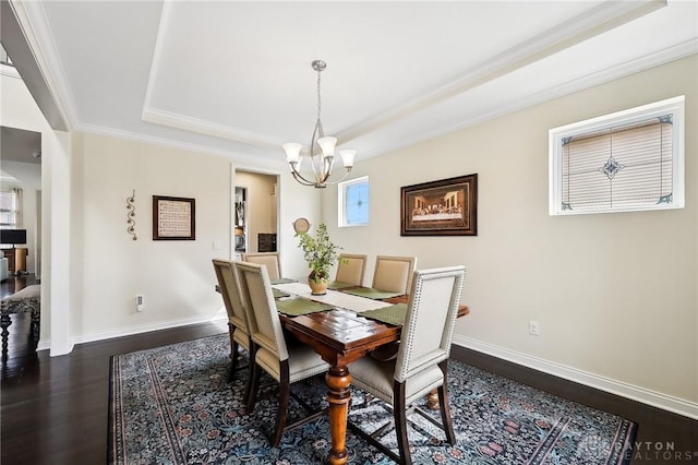 dining room with dark wood finished floors, a raised ceiling, an inviting chandelier, ornamental molding, and baseboards