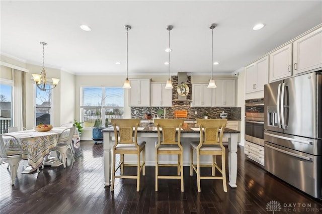 kitchen with appliances with stainless steel finishes, wall chimney range hood, decorative backsplash, dark wood-style floors, and crown molding