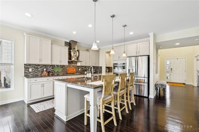 kitchen featuring stainless steel fridge, decorative backsplash, dark wood-style flooring, wall chimney range hood, and a sink