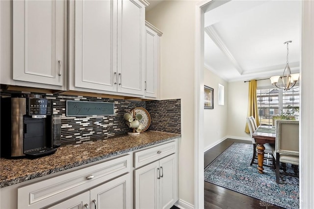 kitchen with dark wood-style floors, decorative backsplash, dark stone counters, a raised ceiling, and crown molding