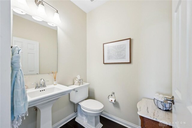 half bath with baseboards, toilet, and wood finished floors