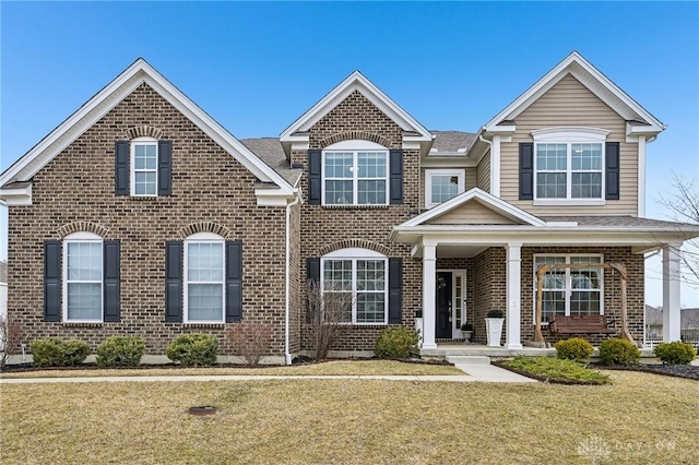 view of front of home featuring covered porch, brick siding, and a front lawn