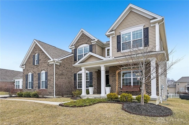 traditional-style home featuring a porch, a front yard, and brick siding