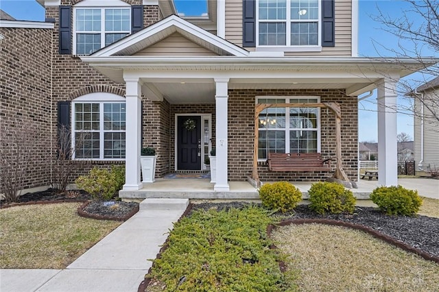 entrance to property featuring a porch and brick siding