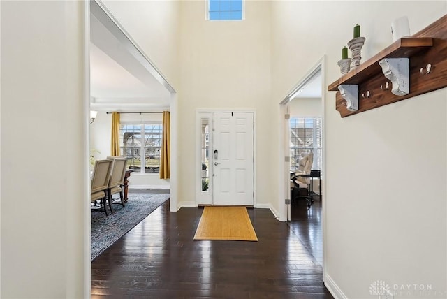 entryway with dark wood finished floors, a towering ceiling, and baseboards