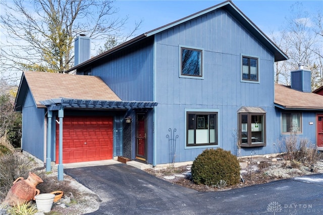 view of front of property with aphalt driveway, an attached garage, a chimney, and a shingled roof