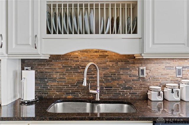 kitchen featuring a sink, tasteful backsplash, white cabinets, and dark stone countertops