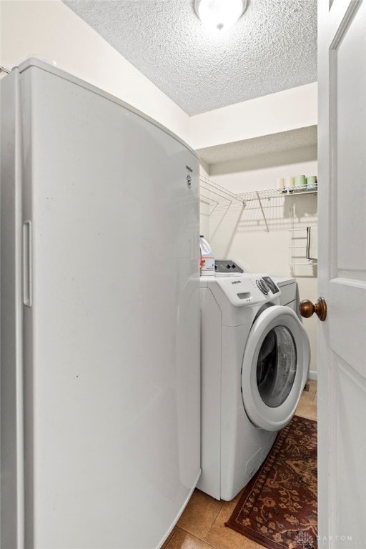 clothes washing area featuring laundry area, washing machine and clothes dryer, light tile patterned flooring, and a textured ceiling