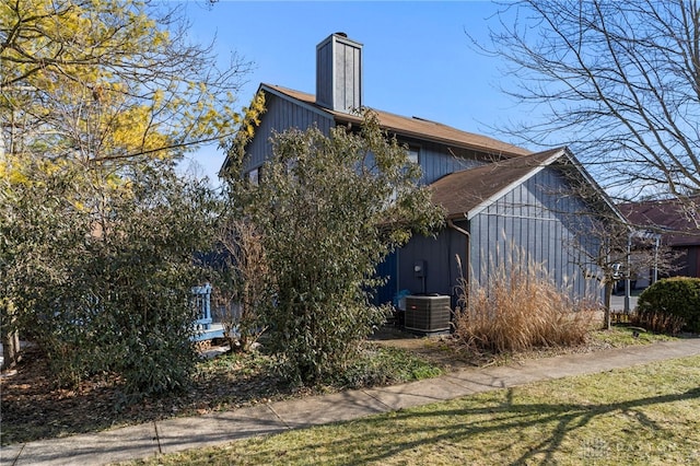 view of side of home featuring roof with shingles, central AC unit, and a chimney