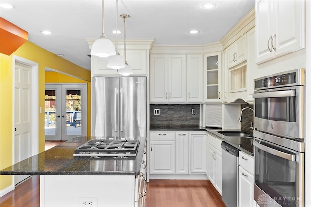 kitchen with a sink, backsplash, wood finished floors, french doors, and appliances with stainless steel finishes