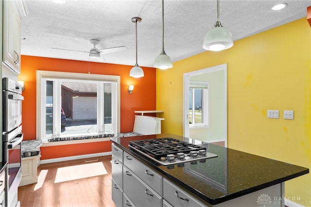 kitchen featuring wood finished floors, a kitchen island, appliances with stainless steel finishes, a textured ceiling, and decorative light fixtures