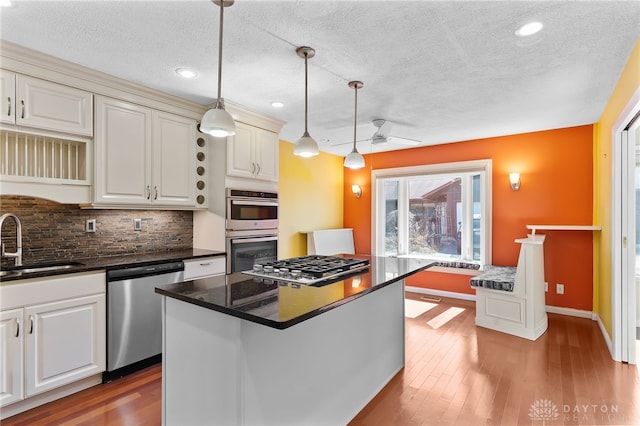 kitchen with a sink, decorative backsplash, appliances with stainless steel finishes, dark countertops, and light wood-type flooring