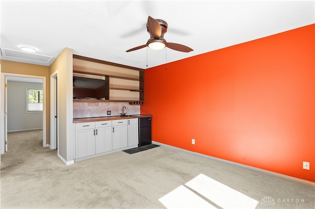 kitchen with baseboards, a sink, butcher block countertops, white cabinets, and light carpet