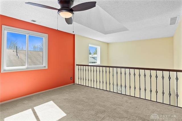 carpeted empty room featuring visible vents, a textured ceiling, baseboards, and a ceiling fan