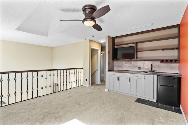 kitchen with a sink, light colored carpet, dark countertops, and a textured ceiling