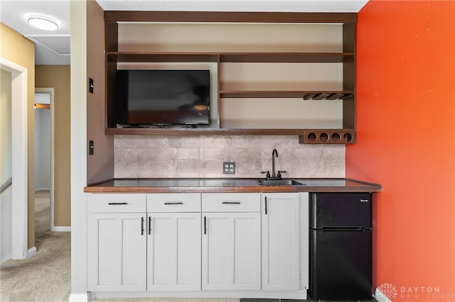 bar featuring decorative backsplash, baseboards, freestanding refrigerator, and a sink