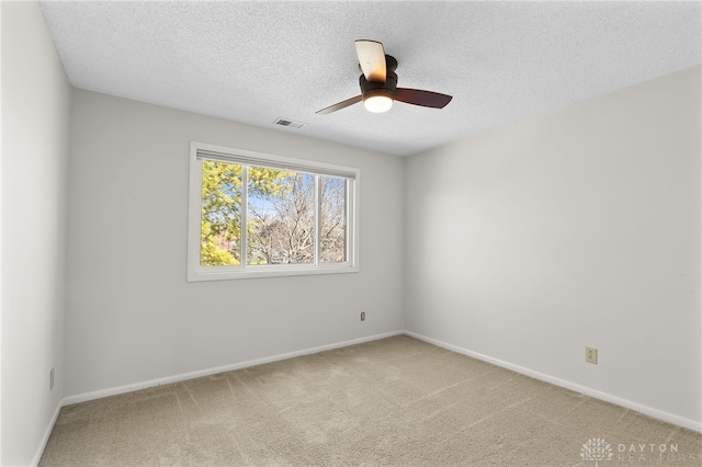 spare room with visible vents, light carpet, a ceiling fan, a textured ceiling, and baseboards