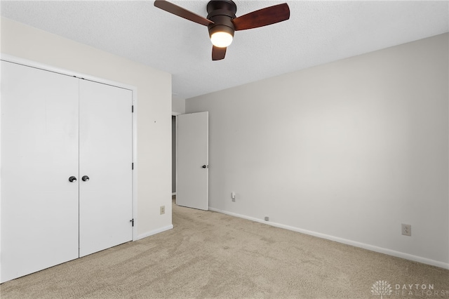 unfurnished bedroom featuring a closet, light colored carpet, a textured ceiling, and baseboards