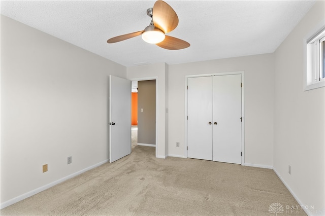 unfurnished bedroom featuring a textured ceiling, a closet, baseboards, light colored carpet, and ceiling fan