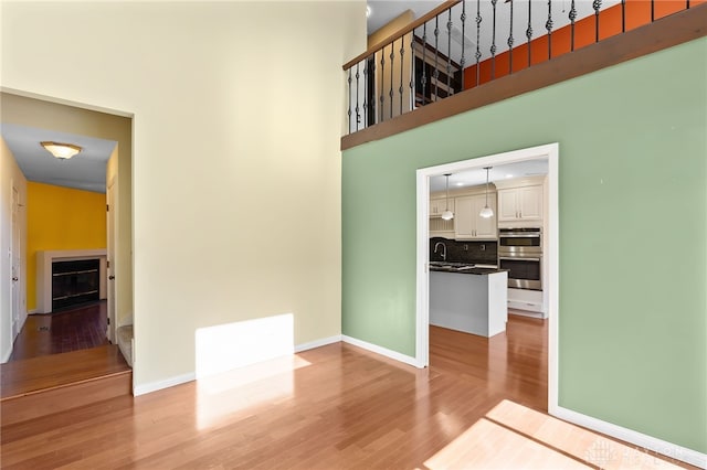 spare room featuring baseboards, a high ceiling, a fireplace, and light wood finished floors