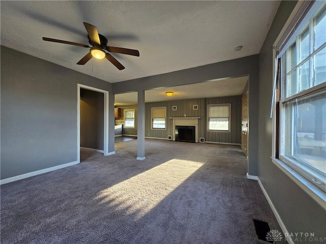 unfurnished living room featuring ceiling fan, a healthy amount of sunlight, and dark colored carpet