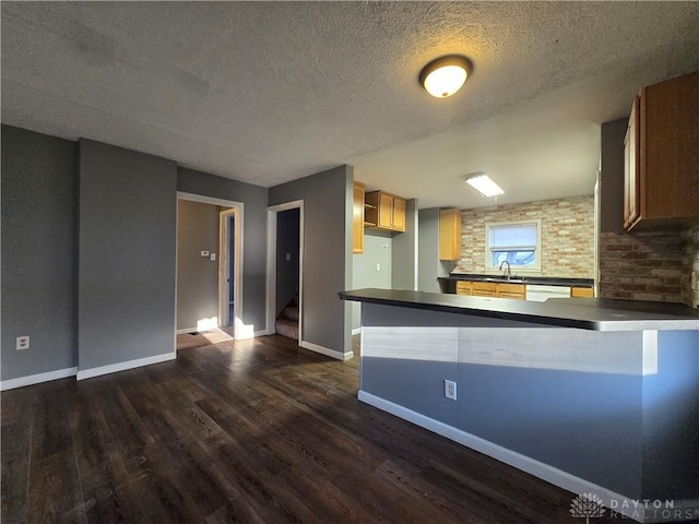 kitchen with sink, a textured ceiling, dark hardwood / wood-style floors, dishwasher, and kitchen peninsula