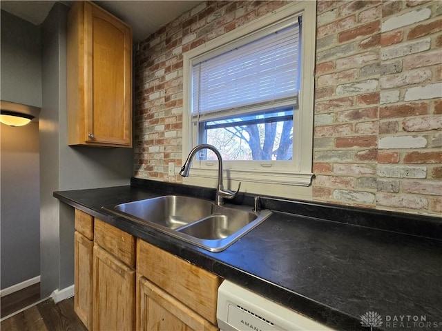 kitchen featuring brick wall, white dishwasher, and sink