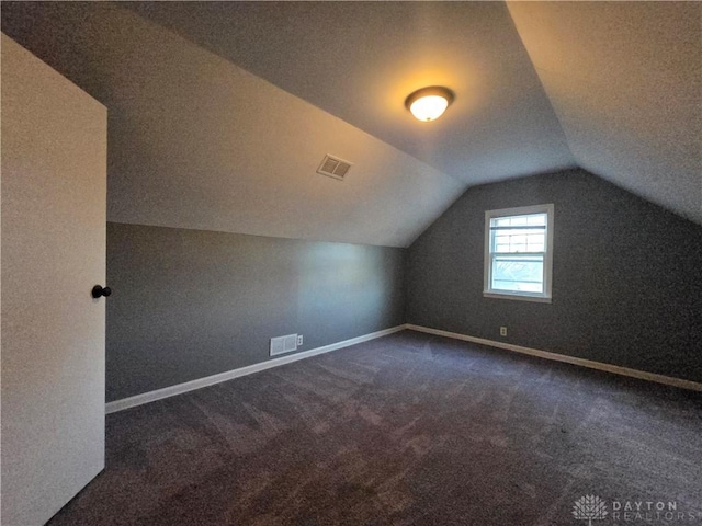 additional living space featuring lofted ceiling and dark colored carpet