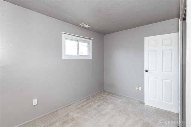 spare room with light colored carpet and a textured ceiling