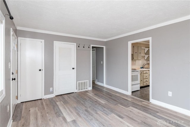 unfurnished bedroom featuring ensuite bath, a textured ceiling, light wood-type flooring, multiple closets, and ornamental molding